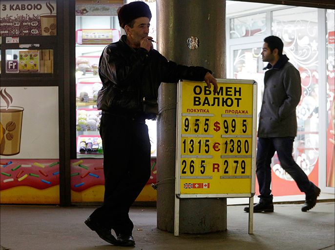 A man smokes near a board showing currency exchange rates in Kiev, February 26, 2014. Ukraine has asked the International Monetary Fund to help prepare a new financial aid program, its central bank chairman said on Wednesday, adding that the new government would soon have its own anti-crisis program ready. He said an anti-crisis plan would be adopted "tomorrow or the day after" and that the central bank would not intervene in the foreign currency market to defend the hryvnia in the coming days. REUTERS/Konstantin Chernichkin (UKRAINE - Tags: BUSINESS)