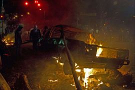 Demonstrators stay next to a car on fire during a protest against the government of Venezuelan President Nicolas Maduro in San Cristobal, capital of the western border state of Tachira, Venezuela, on February 22, 2014