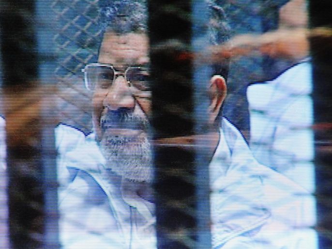 FILE - In this Sunday, Feb. 16, 2014 file photo, Egypt's ousted President Mohammed Morsi in a soundproof barred glass cage is seen on a monitor set up outside a courtroom where Morsi and 35 others are facing charges of conspiring with foreign groups and undermining national security, in Cairo, Egypt. Morsi, toppled in July by the military, faces a host of criminal charges and appeared in court Saturday, Feb. 22, 2014, in a case that charges him and 130 others over prison breaks that freed some 20,000 inmates during the 18-day revolt in 2011 that toppled autocrat Hosni Mubarak. Morsi himself was freed in a prison break before becoming the nation’s first freely elected president. (AP Photo/Mohammed al-Law, File)