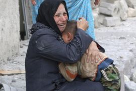 A woman holds a boy as she sits at a site hit by what activists said was a barrel bomb dropped by forces loyal to Syria's President Bashar al-Assad in Aleppo's al-Sakhour district March 6, 2014. REUTERS/Hosam Katan (SYRIA - Tags: POLITICS CIVIL UNREST)