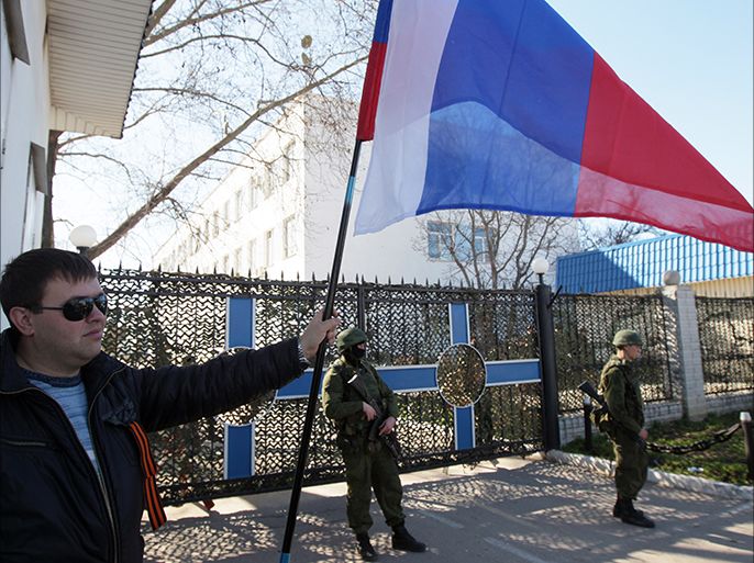 epa04108358 A man holds Russian national flag outside the territory of the Ukrainian naval headquarters in Sevastopol, Ukraine, 03 March 2014. The Russian army reportedly occupied key sites in the autonomous region of Crimea, where a majority of the population is ethnic Russian. Troops surrounded several small military outposts and demanded Ukrainian troops disarm.  EPA/ZURAB KURTSIKIDZE