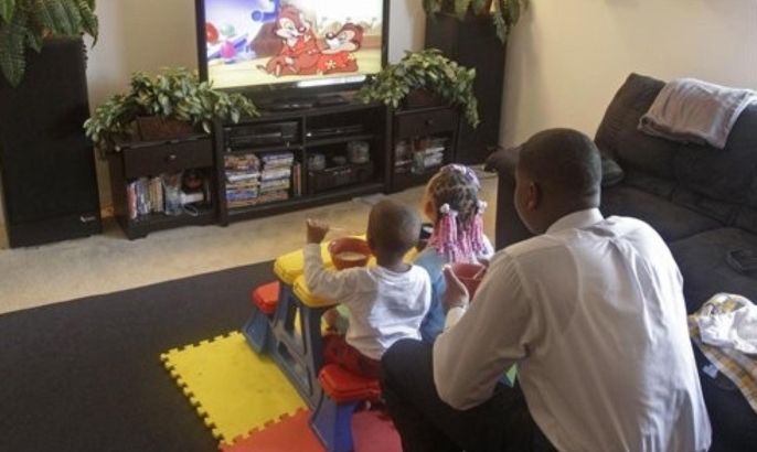 In this Wednesday, May 18, 2011 photo, Adrian McLemore watches television with his niece A'Rayiah McLemore, 4, and nephew Tyiaun Jones, 2, while they eat breakfast inside their apartment, in Dayton, Ohio. Once a foster child himself, McLemore took custody of the children two years ago when his sister was forced to give them up.