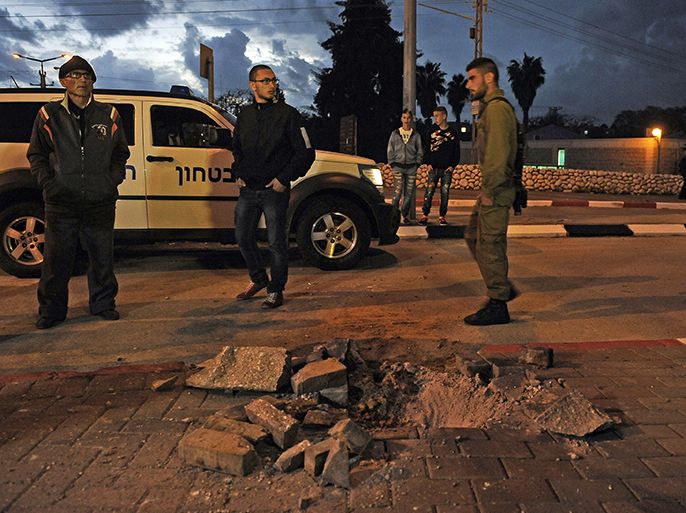 Israeli soldiers and civilians stand next to a hole caused by a rocket launched from the Gaza strip, in the Israeli city of Sderot in the southern Negev desert on March 12, 2014. Islamic Jihad militants in Gaza fired more than 50 rockets at southern Israel, in what it said was a response to an Israeli air strike the day before which killed three of its militants in southern Gaza. AFP