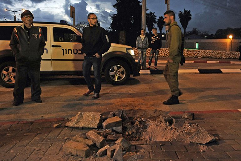 Israeli soldiers and civilians stand next to a hole caused by a rocket launched from the Gaza strip, in the Israeli city of Sderot in the southern Negev desert on March 12, 2014. Islamic Jihad militants in Gaza fired more than 50 rockets at southern Israel, in what it said was a response to an Israeli air strike the day before which killed three of its militants in southern Gaza. AFP