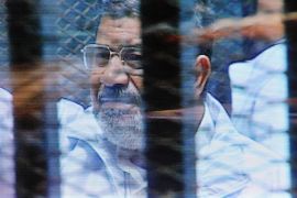 FILE - In this Sunday, Feb. 16, 2014 file photo, Egypt's ousted President Mohammed Morsi in a soundproof barred glass cage is seen on a monitor set up outside a courtroom where Morsi and 35 others are facing charges of conspiring with foreign groups and undermining national security, in Cairo, Egypt. Morsi, toppled in July by the military, faces a host of criminal charges and appeared in court Saturday, Feb. 22, 2014, in a case that charges him and 130 others over prison breaks that freed some 20,000 inmates during the 18-day revolt in 2011 that toppled autocrat Hosni Mubarak. Morsi himself was freed in a prison break before becoming the nation’s first freely elected president. (AP Photo/Mohammed al-Law, File)