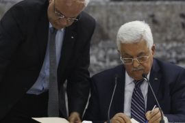 Palestinian chief negotiator Saeb Erekat (L) helps Palestinian President Mahmoud Abbas as he signs international conventions during a meeting with Palestinian leadership in the West Bank City of Ramallah April 1, 2014. Abbas signed more than a dozen international conventions on Tuesday citing anger at Israel's delay of a prisoner release, in a move jeopardised U.S. efforts to salvage fragile peace talks. REUTERS/Mohamad Torokman (WEST BANK - Tags: POLITICS)