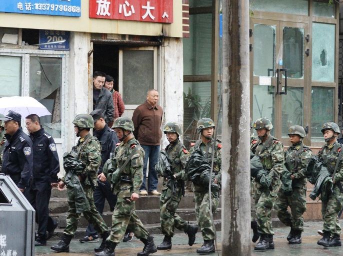 In this May 22, 2014 photo, armed policemen patrol past buildings whose windows were damaged by an explosion in Urumqi, northwest China's Xinjiang region. Attackers hurled bombs from two SUVs that plowed through shoppers at a busy street market in the region on Thursday, killing dozens and wounding more than 90. (AP Photo/Kyodo News) JAPAN OUT, MANDATORY CREDIT