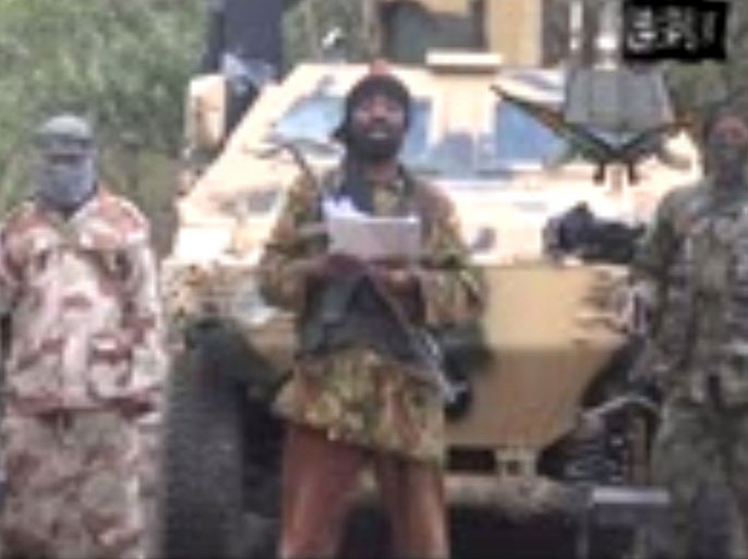A grab made on May 5, 2014 from a video obtained by AFP shows the leader of the Islamist extremist group Boko Haram Abubakar Shekau (C) delivering a speech. Shekau vowed to sell hundreds of schoolgirls kidnapped in northern Nigeria three weeks ago, in a new video obtained on May 5 by AFP. "I abducted your girls. I will sell them in the market, by Allah," he said, after reports that some of the 223 girls still missing may have been sold as brides across Nigeria's border with Chad and Cameroon for as little as $12. Shekau added that the abduction had caused outrage "because we are holding people (as) slaves". AFP PHOTO / BOKO HARAM