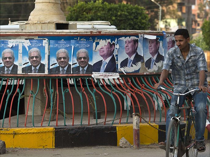 An Egyptian man rides a bicycle past campaign posters of leftist presidential candidate Hamdeen Sabbahi (L) and of Egyptian ex-army chief and leading presidential candidate Abdel Fattah al-Sisi (R) in the town of Dekernss near the Nile Delta City of Mansura some 120 km north of Cairo on May 15, 2014. Sisi is expected to win the May 26-27 election against his only rival, Sabbahi, amid cal