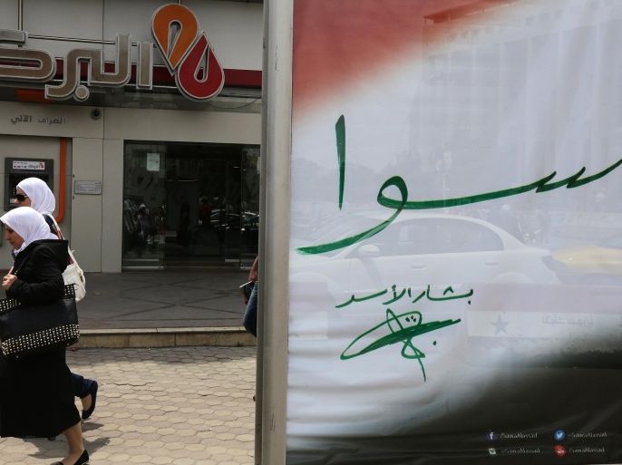 Syrian women walk past an election campaign billboard bearing President Bashar al-Assad's signature and the word 'together' written in Arabic on May 11, 2014 in the capital Damascus. Campaigning began today for Syria's June 3 presidential election expected to return Bashar al-Assad to power, as the regime marked a symbolic victory with the exit of rebels from Homs. AFP PHOTO / LOUAI BESHARA