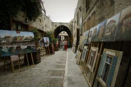 Tourists look at paintings displayed at an old market in the Lebanese ancient port city of Byblos on August 10, 2010.