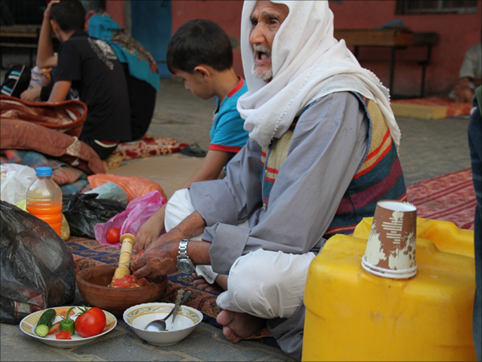 ‪مسن نازح يُعد طعام الإفطار بإحدى مدارس الأونروا بمخيم خان يونس‬ (الجزيرة)