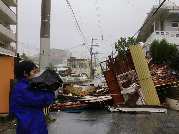 epa04305019 A reporter stands next to a wooden house hosting a restaurant obstructing a street after it collapsed due to the strong generated by typhoon Neoguri in Matsugawa district of Naha city, on the island of Okinawa, southern Japan, 08 July 2014. Residents on southern Japanese islands are advised to be on maximum alert early on 08 July 2014 as a powerful typhoon approached the region. The typhoon is expected to pick up more power before it makes landfall, the Japan Meteorological Agency said, as it issued an storm surge warning for Miyako Island in the southern prefecture of Okinawa and neighbouring islets. EPA/HITOSHI MAESHIRO