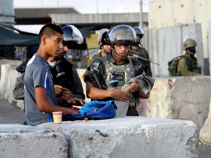 A Palestinian youth has his bag checked by Israeli soldiers as he crosses Qalandia checkpoint on his way to Al-Aqsa mosque in the Old city of Jerusalem to attend the last Friday prayer in the fasting month of Ramadan, 25 July 2014. The street is full of stones which were hurled in clashes between Palestinians and Israeli security forces. Israeli military authorities limited the age of Muslims from West Bank allowed to enter Al-Aqsa Mosque by the age of 50 for men and 40 for women with a very low number of Palestinians manage to arrive at the crossing compared to previous years because of the tightening on Palestinians movement from West Bank to Jerusalem.