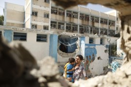 A Palestinian man pictured through a damaged classroom carries a boy as he walks at a United Nations-run school sheltering Palestinians displaced by an Israeli ground offensive, that witnesses said was hit by Israeli shelling, in Jebalya refugee camp in the northern Gaza Strip July 30, 2014. Israeli shelling killed at least 15 Palestinians sheltering in a school in Gaza's biggest refugee camp on Wednesday, the Health Ministry said, as Egyptian mediators prepared a revised proposal to try to halt more than three weeks of fighting. Some 3,300 Palestinians, including many women and children, were taking refuge in the building in Jebalya refugee camp when it came under fire around dawn, the United Nations Relief and Works Agency (UNRWA) said. An Israeli military spokeswoman said militants had fired mortar bombs from the vicinity of the school and troops shot back in response. The incident was still being reviewed. Israel launched its offensive in response to rocket salvoes fired by Gaza's dominant Hamas Islamists and their allies. REUTERS/Suhaib Salem (GAZA - Tags: POLITICS CIVIL UNREST CONFLICT)