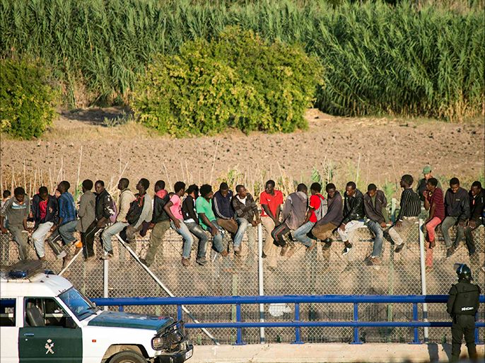 African migrants climb a border fence, as Spanish Civil Guard officers stand under them, during a latest attempt to cross into Spanish territory, between Morocco and Spain's north African enclave of Melilla August 12, 2014. Around 500 people stormed the border, where 25 of them passed the fence and they are currently held at CETI, the short-stay immigrant centre, according to local authorities. REUTERS/Jesus Blasco de Avellaneda (SPAIN - Tags: SOCIETY IMMIGRATION CRIME LAW)