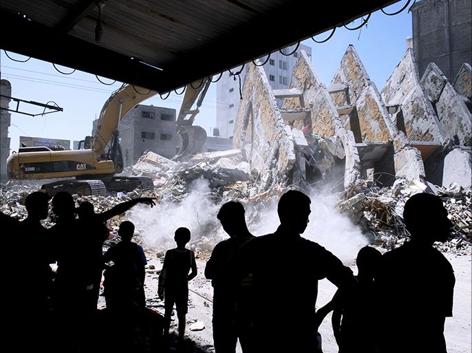 Palestinian men watch as the rubble left from a collapsed building that was targeted by Israeli air strikes overnight is cleared off a street in Gaza City on August 26, 2014. Israeli air raids on Gaza City killed two Palestinians early in the morning while scores more were wounded when warplanes bombed two high-rise residential blocks, medics and witnesses said. The raids came as Israel stepped up the pressure on Hamas on day 50 of a bloody confrontation which began on July 8 and has claimed the lives of more than 2,100 Palestinians and 68 on the Israeli side. AFP PHOTO/ROBERTO SCHMIDT