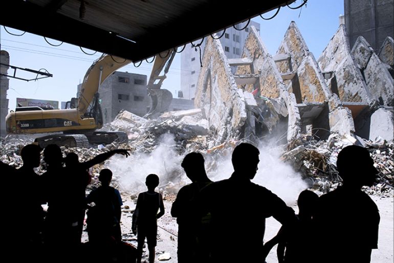 Palestinian men watch as the rubble left from a collapsed building that was targeted by Israeli air strikes overnight is cleared off a street in Gaza City on August 26, 2014. Israeli air raids on Gaza City killed two Palestinians early in the morning while scores more were wounded when warplanes bombed two high-rise residential blocks, medics and witnesses said. The raids came as Israel stepped up the pressure on Hamas on day 50 of a bloody confrontation which began on July 8 and has claimed the lives of more than 2,100 Palestinians and 68 on the Israeli side. AFP PHOTO/ROBERTO SCHMIDT
