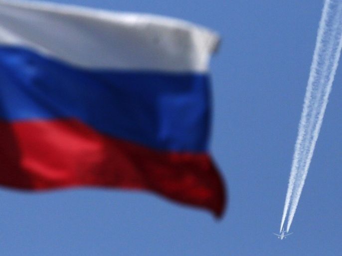 A contrail left by a passenger plane is seen behind a Russian state flag as it passes over the Siberian city of Krasnoyarsk, August 7, 2014. Russian Prime Minister Dmitry Medvedev said on Thursday that Moscow was considering banning transit flights by airlines from the European Union and the United States to the Asia-Pacific region. REUTERS/Ilya Naymushin (RUSSIA - Tags: POLITICS TRANSPORT BUSINESS)