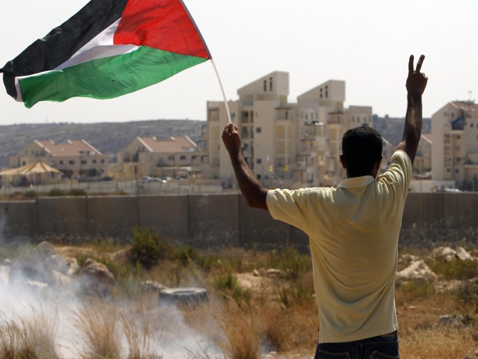 ‪متظاهر يرفع العلم الفلسطيني خلال اشتباكات مع قوات الاحتلال ببلعين‬ (غيتي)