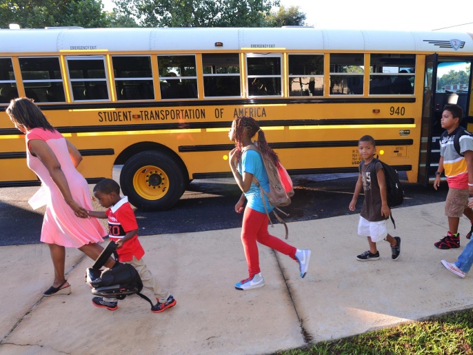 Students walk off of a bus on the first full day of school for most Northeast Florida students, Monday, Aug. 18, 2014. Arlington Heights Elementary in Jacksonville, Fla. started seeing students arrive at 7:30, an hour before the scheduled start of the day and by 8am the main office was crowded with parents and kids trying to get registered for school. Assistant Principal Regina Thomas holds kindergartner Malcolm McCord's hand as she leads the students from their bus for the 8am first bell that allows students into the school. (AP Photo/The Florida Times-Union, Bob Mack)