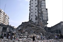 Palestinians walk at the base of what used to be a high rise apartment building in Gaza City that was targeted by Israeli air strikes overnight on August 26, 2014
