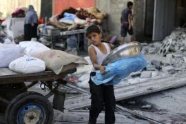 A Palestinian boy carries belongings near his family's damaged house, which witnesses said was hit by an Israeli air strike, in Rafah in the southern Gaza Strip August 26, 2014. Israeli air strikes launched before dawn on Tuesday killed two Palestinians and destroyed much of one of Gaza's tallest apartment and office buildings, setting off huge explosions and wounding 20 people, Palestinian health officials said. Israel had no immediate comment on the attacks that took place as Egyptian mediators stepped up efforts to achieve an elusive ceasefire to end seven weeks of fighting. Israel launched an offensive on July 8, with the declared aim of ending rocket fire into its territory. REUTERS/Ibraheem Abu Mustafa (GAZA - Tags: POLITICS CIVIL UNREST)