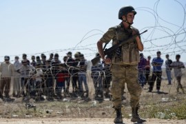 A Turkish soldier stands guard as Syrian Kurds wait behind the border fence near the southeastern town of Suruc in Sanliurfa province, September 21, 2014. Kurdish militants in Turkey have issued a new call to arms to defend a border town in northern Syria from advancing Islamic State fighters, and the Turkish authorities and United Nations prepared on Sunday for a surge in refugees. About 70,000 Syrian Kurds have fled into Turkey since Friday as Islamic State fighters seized dozens of villages close to the border and advanced on the frontier town of Ayn al-Arab, known as Kobani in Kurdish. REUTERS/Stringer (TURKEY - Tags: POLITICS MILITARY CIVIL UNREST CONFLICT SOCIETY IMMIGRATION)