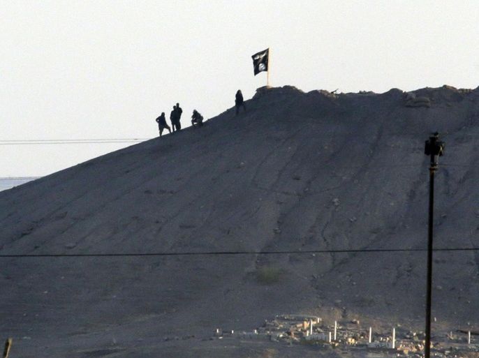 In this image shot with an extreme telephoto lens and through haze from the outskirts of Suruc at the Turkey-Syria border, militants with the Islamic State group are seen after placing their group's flag on a hilltop at the eastern side of the town of Kobani, Syria, where fighting had been intensified between Syrian Kurds and the militants of Islamic State group, Monday, Oct. 6, 2014. Kobani, also known as Ayn Arab and its surrounding areas have been under attack since mid-September, with militants capturing dozens of nearby Kurdish villages. The flag is indicating that the jihadists may have regrouped and broken through the Kurdish lines. (AP Photo/Lefteris Pitarakis)