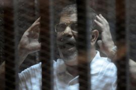 Egypt's deposed Islamist president Mohamed Morsi gestures inside the defendants cage during his trial at the police academy in Cairo on October 14, 2014. Morsi is on trial in several cases and faces a death sentence if convicted of espionage and terrorism related charges. AFP PHOTO / STR