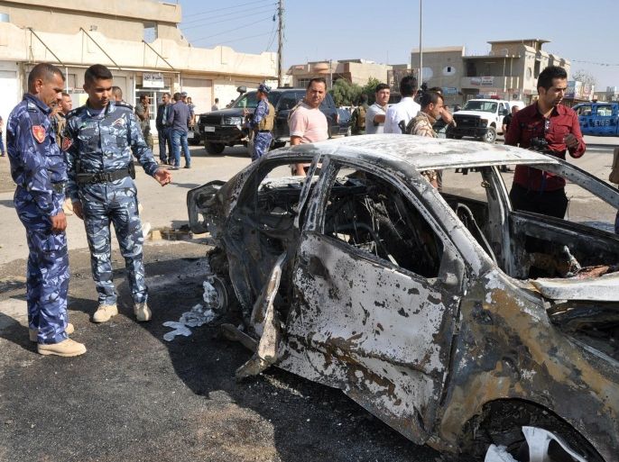 Members of the Iraqi security forces and civilians look at a burnt-out vehicle following a motorcycle bomb attack targeting a police patrol east of the northern Iraqi city of Kirkuk on October 13, 2014. AFP PHOTO / MARWAN IBRAHIM