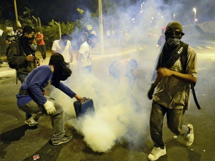 A violent demonstrator covers a tear gaz can fired by the police in Belo Horizonte, Brazil on June 26, 2013, during a protest outside the Mineirao stadium where Brazil was playing the semi final match of the Confederations Cup against Uruguay. The protests come as Brazil hosts a dry run for the World Cup, called the Confederations Cup.