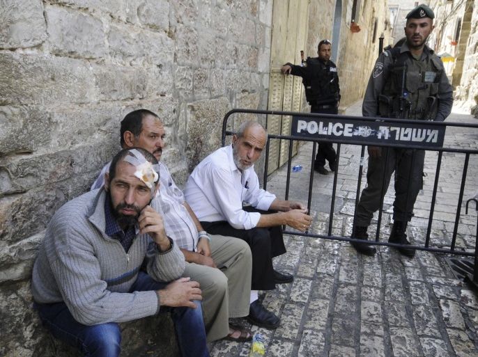 A Palestinian injured in clashes sits next to Israeli border policeman after police closed access to Al-Aqsa mosque in Jerusalem on Wednesday, Oct. 8, 2014. The violence began as the masked Palestinians threw rocks at tourists and Jewish Israelis who visited the site early Wednesday, hours before the start of the Jewish festival of Sukkot at nightfall, a police spokesperson said. Palestinians view such visits as a provocation and often respond violently. (AP Photo/Mahmoud Illean)