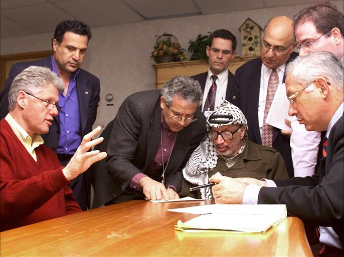 US President Bill Clinton (L) holds a late-night meeting with Palestinian leader Yasser Arafat (C) and Israeli Prime Minister Benjamin Netanyahu (R) near midnight 22 October at the Wye River Conference Center, MD. Also present are (from L-R): note taker Nabil Abu Rudineh (2nd L), translator Gamal Halel (3rd L), PLO official Nabil Shaath (3rd R), and Danny Naveh (function unknown). The man rear center standing is unidentified.