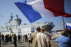 A man holds up a French flag during a demonstration supporting a contract to deliver the Mistral-class helicopter carrier Vladivostok warship to Russia (seen in the background), at the STX Les Chantiers de l'Atlantique shipyard site in Saint-Nazaire, September 7, 2014. French President Francois Hollande said on Thursday that a ceasefire and a political settlement in Ukraine were conditions for France to deliver the warship it has built for Russia. Hollande told reporters on the sidelines of a NATO summit that the 2011 contract to supply two Mistral-class helicopter carriers was neither canceled nor suspended, but the conditions for delivering the first ship - due in October 2014 - were not ripe. The banner reads, "Hollande wants to kill Saint-Nazaire, we said No". REUTERS/Stephane Mahe (FRANCE - Tags: MILITARY POLITICS CIVIL UNREST)