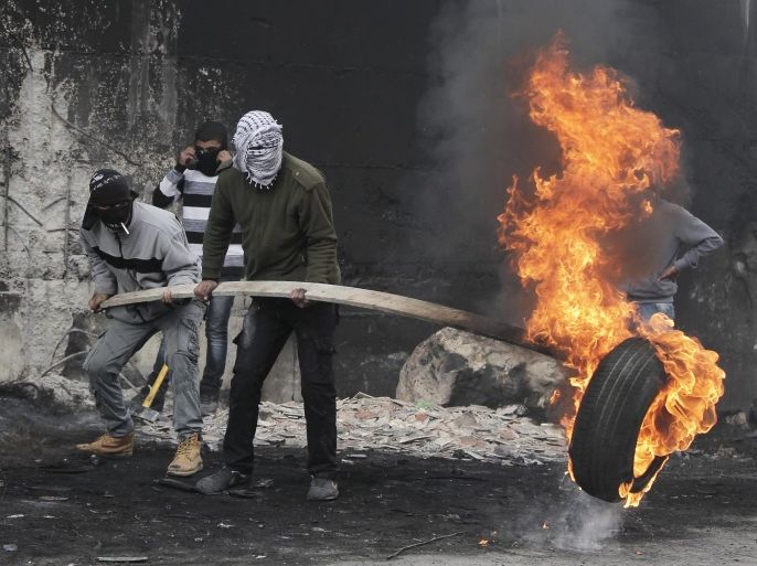 Palestinian protesters burn a tyre in front of Israel's controversial barrier that separates the West Bank town of Abu Dis from Jerusalem on November 17, 2014. A Palestinian bus driver, whose family lives in Abu Dis, was found hanged in his vehicle in west Jerusalem overnight, in what Israeli police said was an apparent suicide but a colleague said looked like murder. AFP PHOTO / AHMAD GHARABLI