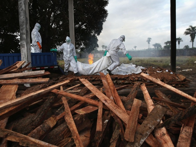 ‪عمال يجهزون جثث موتى إيبولا لحرقها‬ (غيتي)