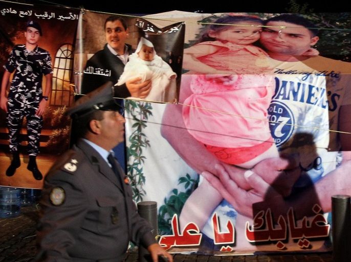 A Lebanese policeman walks past posters showing one of the Lebanese soldiers, who was kidnapped by Islamic militants, carrying his daughter, on a tent occupied by his family outside the government palace in downtown Beirut as they hold a sit-in late on December 5, 2014. The Al-Qaeda-linked Syrian extremist group the Al-Nusra front claimed to have killed a captured Lebanese soldier to avenge the arrest of the daughter and former wife of Abu Bakr al-Baghdadi, who leads the Islamic State jihadist group. AFP PHOTO/ANWAR AMRO