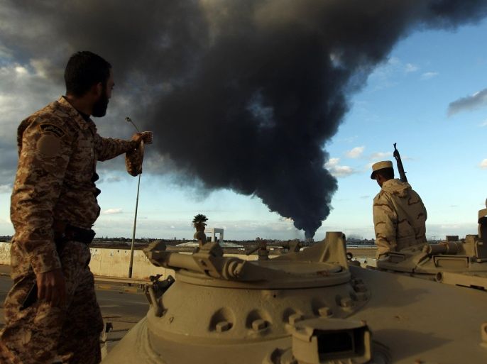 Members of the Libyan army stand on a tank as heavy black smoke rises from the city's port in the background after a fire broke out at a car tyre disposal plant during clashes against Islamist gunmen in the eastern Libyan city of Benghazi on December 23, 2014. Forces loyal to former general Khalifa Haftar and to internationally recognised Prime Minister Abdullah al-Thani have been battling for weeks against Islamists who have taken control of much of Libya's second city, and the capital Tripoli. AFP PHOTO / ABDULLAH DOMA