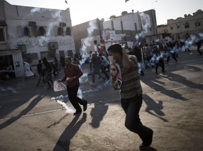 Bahraini protestors run for cover from tear gas during clashes with riot police following a protest against the arrest of the head of the banned Shiite opposition movement Al-Wefaq, Sheikh Ali Salman (on the posters) on January 1, 2015 in Bilad al-Qadeem, a suburb of Manama. Bahrain has urged Iran to look at its own human rights record after it called for the immediate release of Ali Salman. AFP PHOTO / MOHAMMED AL-SHAIKH