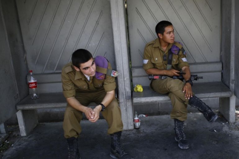 Israeli soldiers wait at a bus stop at Kibbutz Yad Mordechai near the border with northern Gaza August 28, 2014. An open-ended ceasefire in the Gaza war held on Wednesday as Prime Minister Benjamin Netanyahu faced strong criticism in Israel over a costly conflict with Palestinian militants in which no clear victor has emerged. REUTERS/Amir Cohen (ISRAEL - Tags: POLITICS CONFLICT CIVIL UNREST MILITARY)
