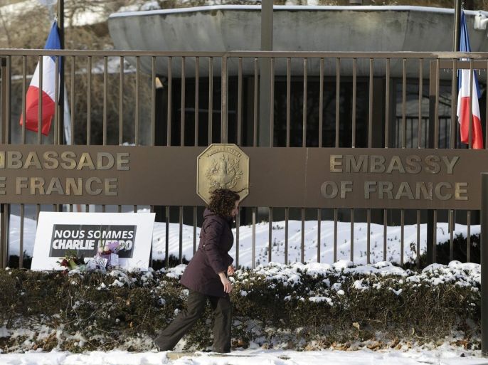 A woman from the French Embassy walks away after placing a sign that reads "We are all Charlie Hebdo" in Washington January 7, 2015. Hooded gunmen stormed the Paris offices of a satirical magazine known for lampooning Islam and other religions on Wednesday, killing at least 12 people in the most deadly militant attack on French soil in decades. French flags fly at half staff, rear. REUTERS/Gary Cameron (UNITED STATES - Tags: POLITICS CRIME LAW CIVIL UNREST)