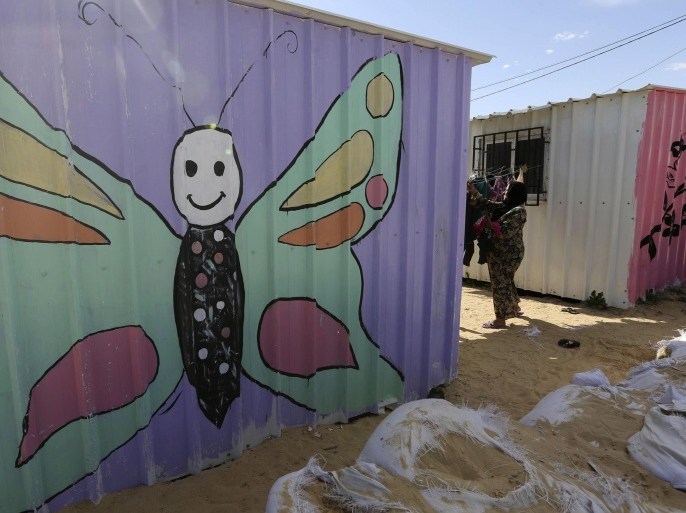 A Palestinian woman, who lives in a container acting as a temporary replacement for her house that witnesses said was destroyed by Israeli shelling during a 50- day-war last summer, collects laundry on a rope outside her mobile shelter at the east of Khan Younis in the southern Gaza Strip February 7, 2015. The containers were painted by some Palestinian artists to add colour to the place and to amuse young children. Picture taken February 7, 2015. REUTERS/Ibraheem Abu Mustafa (GAZA - Tags: POLITICS CONFLICT SOCIETY CIVIL UNREST)