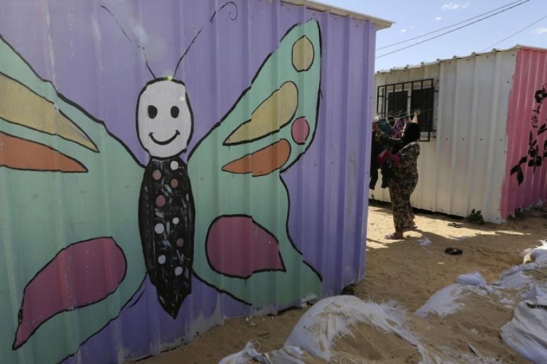 A Palestinian woman, who lives in a container acting as a temporary replacement for her house that witnesses said was destroyed by Israeli shelling during a 50- day-war last summer, collects laundry on a rope outside her mobile shelter at the east of Khan Younis in the southern Gaza Strip February 7, 2015. The containers were painted by some Palestinian artists to add colour to the place and to amuse young children. Picture taken February 7, 2015. REUTERS/Ibraheem Abu Mustafa (GAZA - Tags: POLITICS CONFLICT SOCIETY CIVIL UNREST)