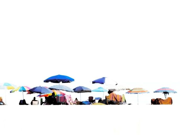 Sunbathers laying on blankets and chairs under sunshades on beach