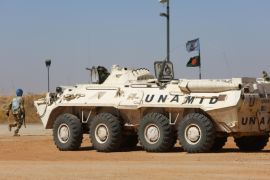 A member of the UN-African Union mission in Darfur (UNAMID) runs past an armoured personnel carrier patrolling near the city of Nyala in Sudan's Darfur on January 12, 2015. Qatar's deputy premier Ahmed bin Abdullah al-Mahmud is on a visit to the war-torn western region of Sudan for the ninth meeting of the committee monitoring the implementation of the Doha Document for Peace Darfur (DDPD). AFP PHOTO / ASHRAF SHAZLY