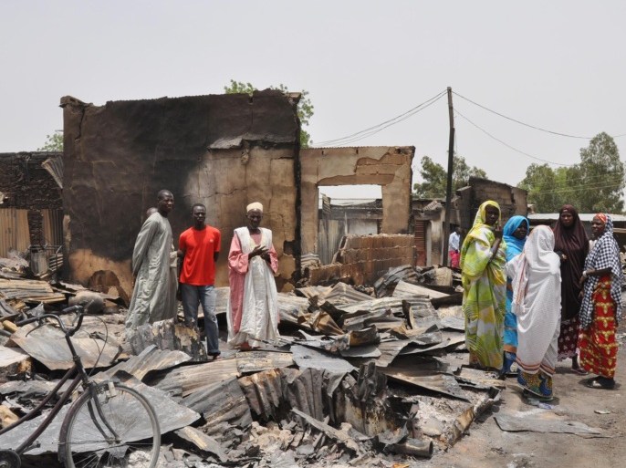 In this photo taken Sunday, May 11, 2014, people stand outside burnt houses following an attack by Islamic militants in Gambaru, Nigeria. Many brutalized residents of the once bustling town of Gamboru said Monday May 12, 2014, they are moving across the border to Cameroon because they cannot trust the Nigerian government to protect them, after repeated attacks by Islamic militants, including an attack a few days ago that killed some hundreds of people with more than 1,000 shops, dozens of homes and 314 trucks and cars bombed and burned out.(AP Photo/Jossy Ola)