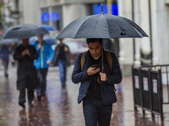 A pedestrian carries an umbrella while checking mobile phone in the rain on Market Street in San Francisco, California, U.S., on Thursday, Dec. 11, 2014. San Francisco is reeling under a Pacific storm that flooded transit stations, grounded flights and left more than 90,000 people without power.