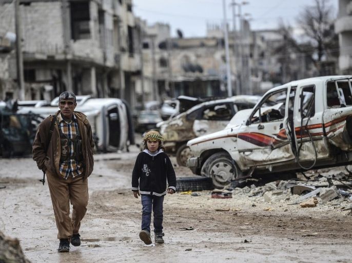 A Kurdish fighter walks with a child in the destroyed Syrian town of Kobane, also known as Ain al-Arab, on January 30, 2015. Kurdish forces recaptured the town on the Turkish frontier on January 26, in a symbolic blow to the jihadists who have seized large swathes of territory in their onslaught across Syria and Iraq. AFP PHOTO/BULENT KILIC