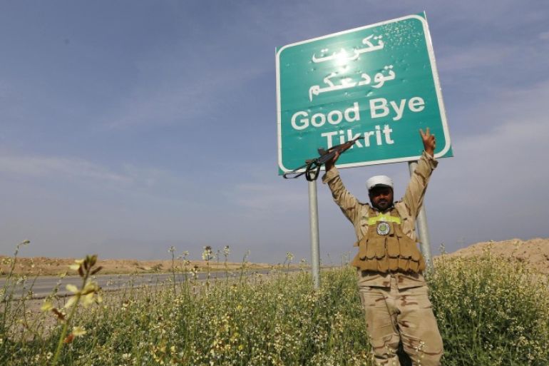 A Shi'ite fighter gestures in front of a billboard on a street in the town of al-Alam March 9, 2015. Just north of Tikrit, home city of executed Sunni former president Saddam Hussein, Iraqi security forces and Shi�ite militia fighters began an offensive against Islamic State to regain control over the town of al-Alam. REUTERS/Thaier Al-Sudani (IRAQ - Tags: POLITICS CIVIL UNREST CONFLICT)